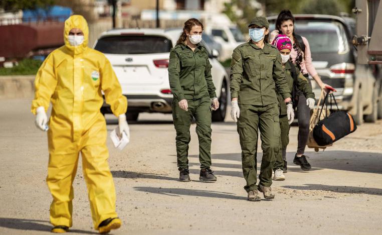 Members of Kurdish security and the Kurdish Red Crescent in protective gear escort a passenger upon arrival from Damascus