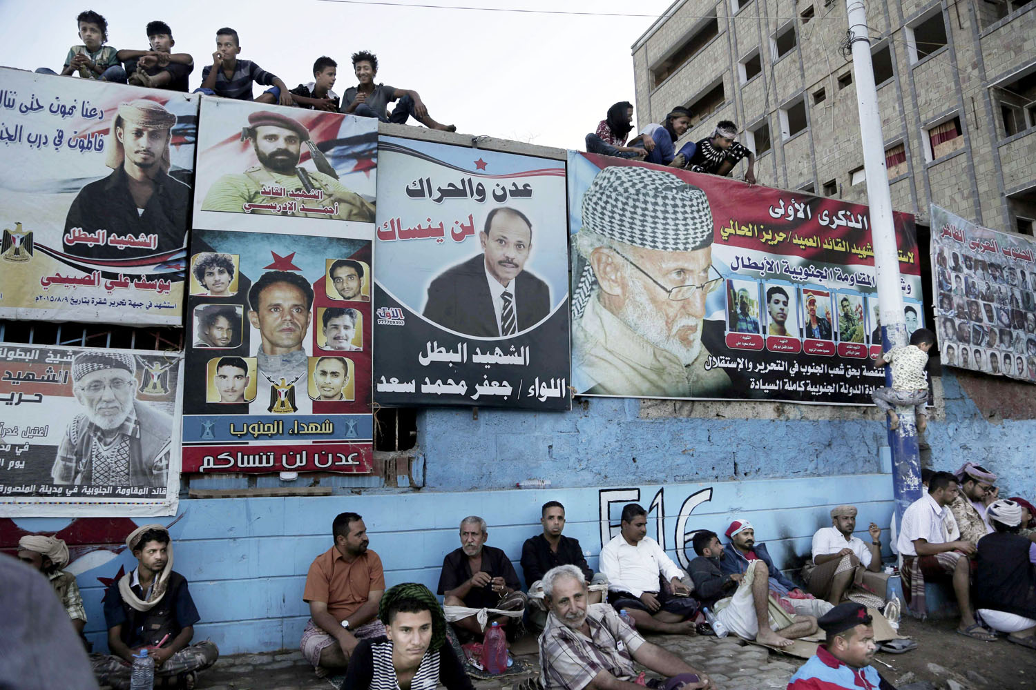 يمنيون في عدن يجلسون امام ملصقات تؤبن قادة المقاومة ضد الاجتياح الحوثي