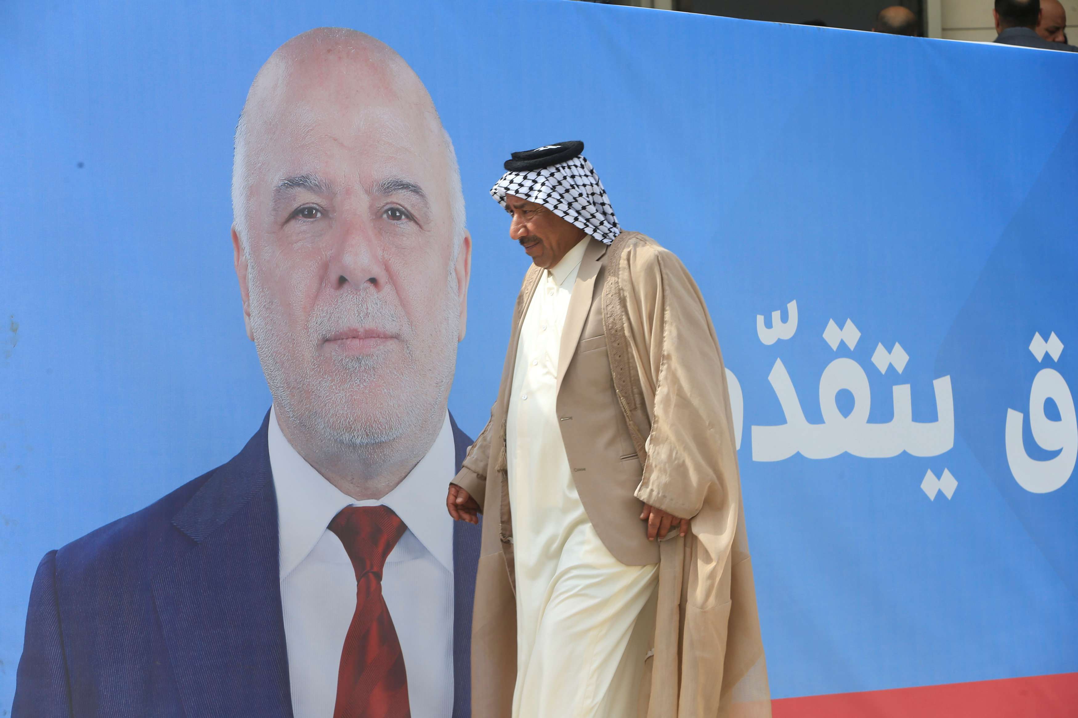عراقي يمر بالقرب من ملصق انتخابي لرئيس الوزراء العراقي حيدر العبادي