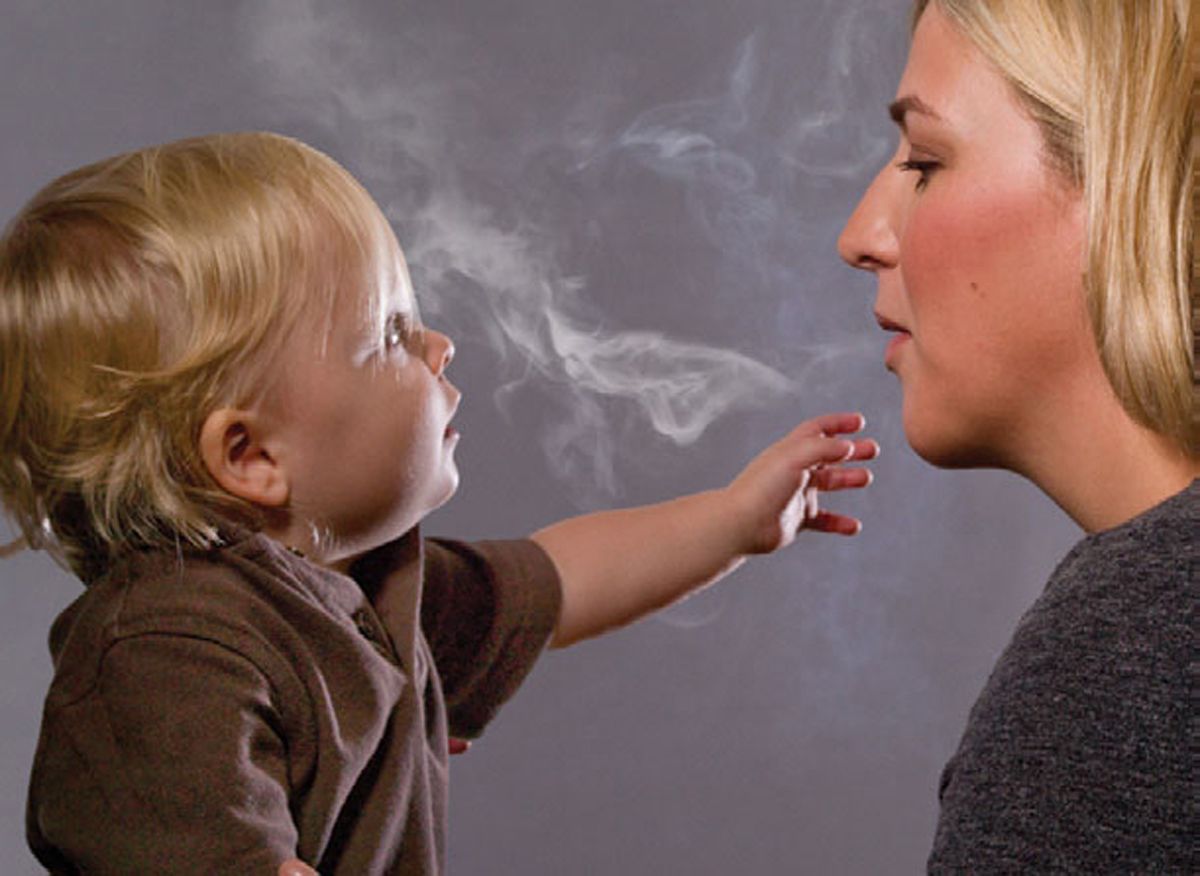مرأة تنفث دخانا قرب طفل 