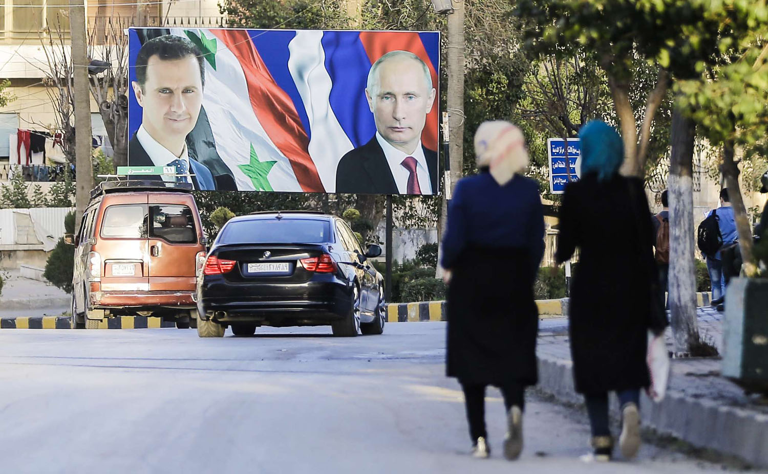 سيدتان سوريتان تمران بالقرب من ملصق كبير للرئيسين بوتين والأسد في دمشق