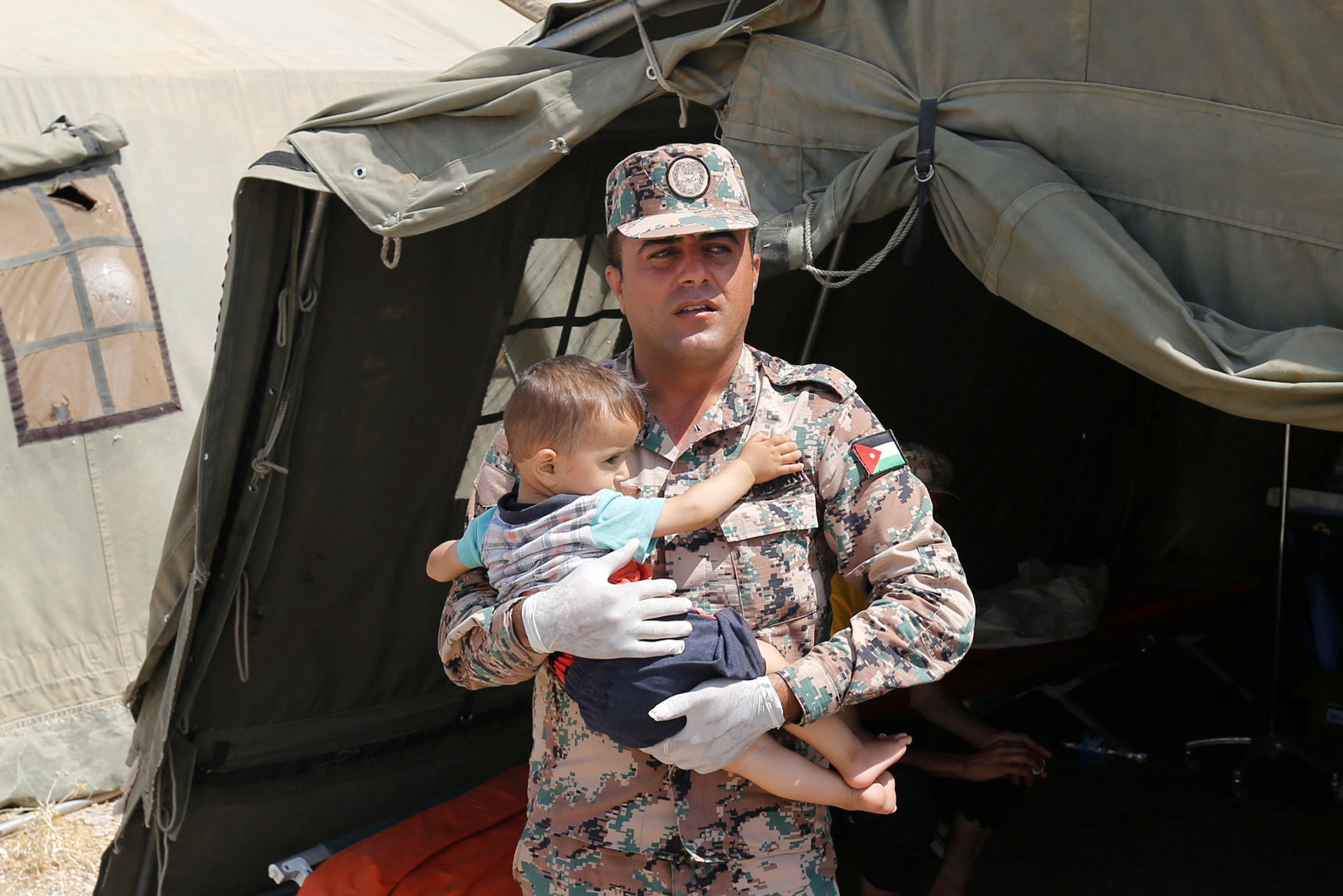 جندي اردني يحمل طفلا سوريا في مخيم للنازحين