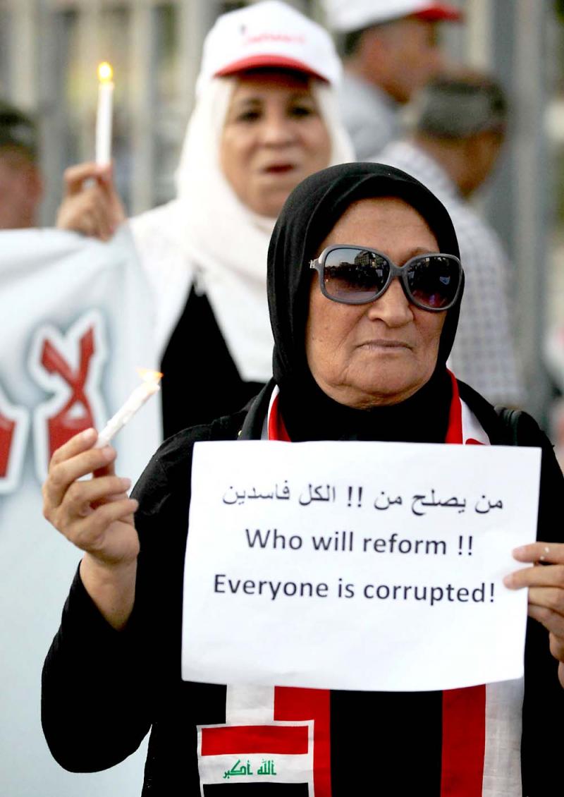 An Iraqi woman holds a sign and a candle during a demonstration in Baghdad’s Tahrir Square, on July 31