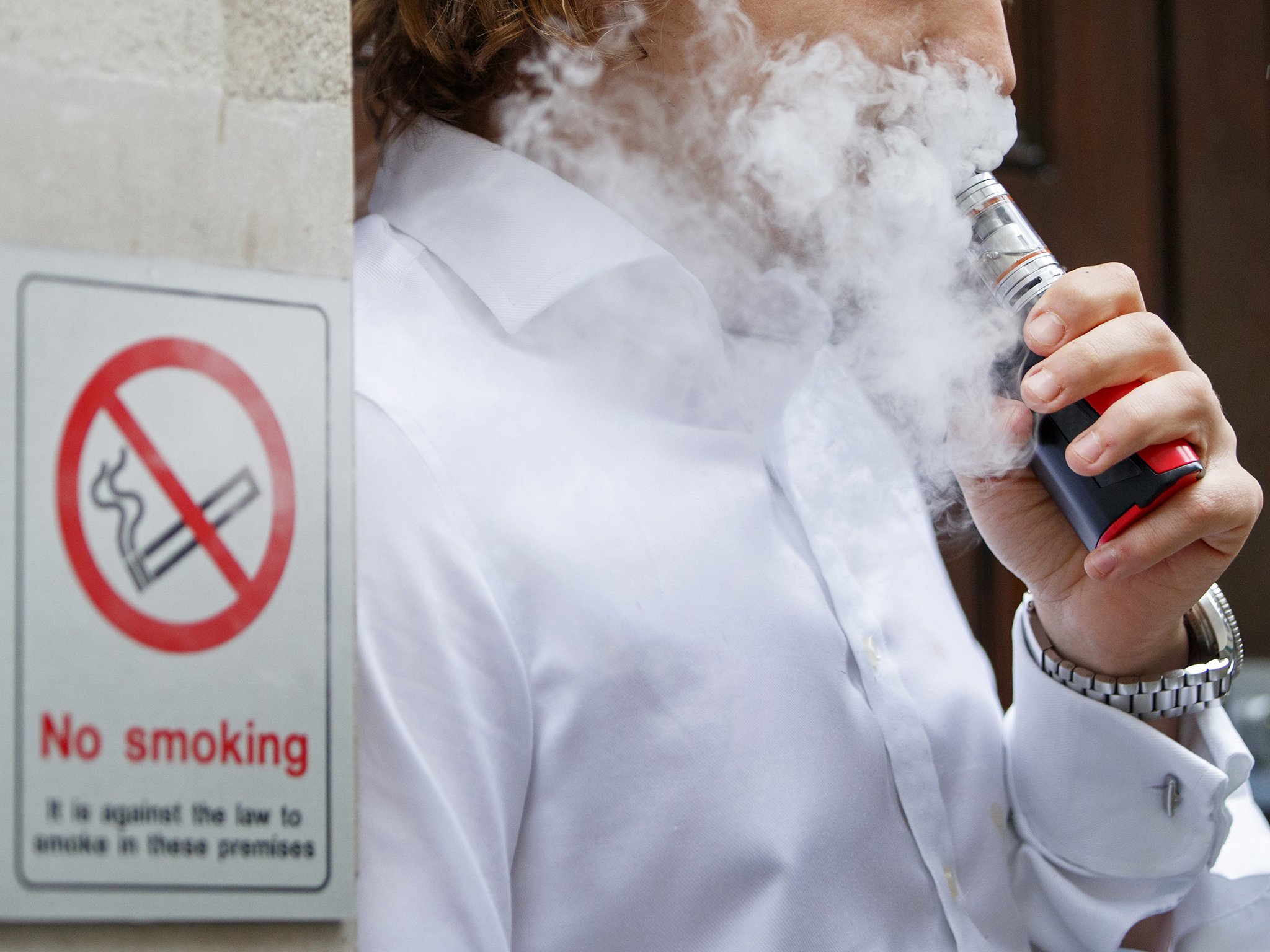 رجل يدخن سجائرا الكترونية قرب لافتة تحظر التدخين
