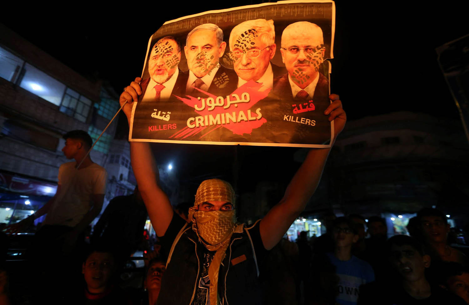 متظاهر فلسطيني في غزة يرفع لافتة تدين القيادات الفلسطينية والإسرائيلية