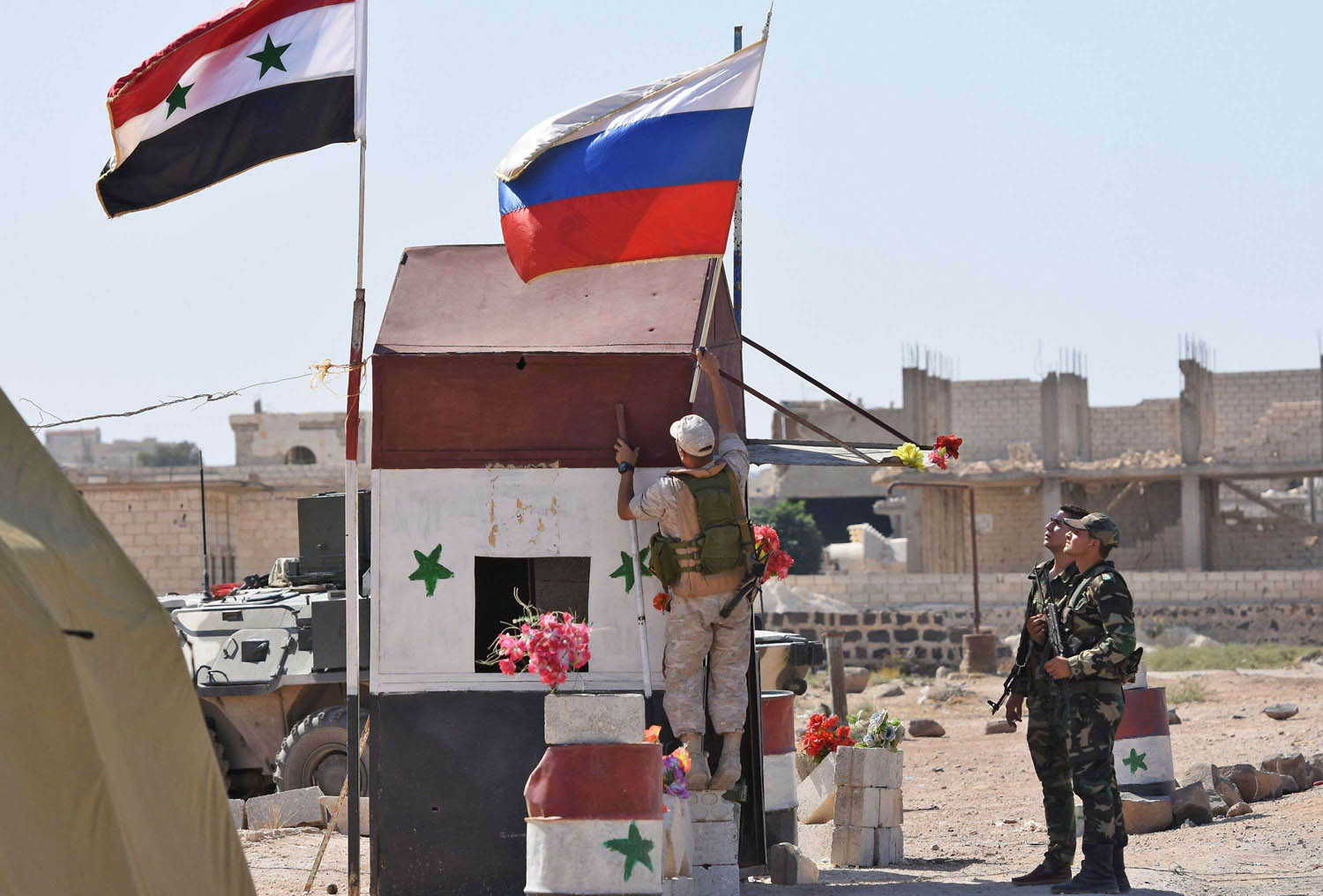 جندي روسي يرفع علم بلاده إلى جانب العلم السوري في أبو الظهور بالقرب من إدلب