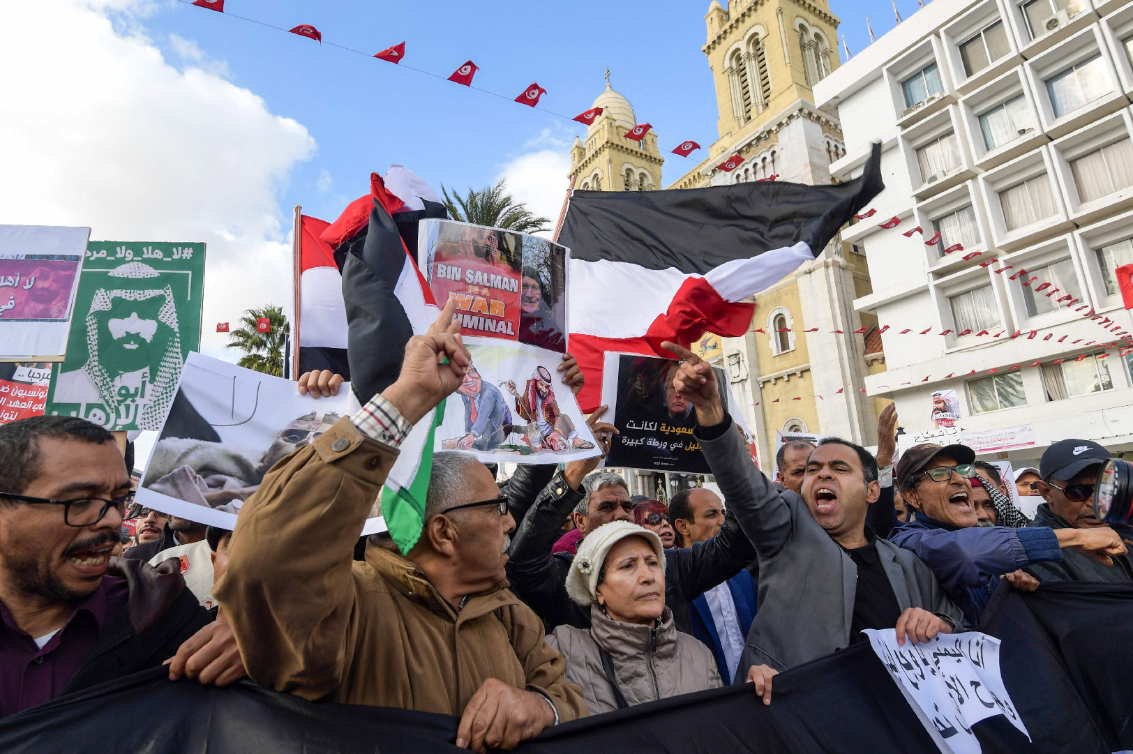 Tunisians shout slogans and hold up signs as they protest against the expected visit of the Saudi Crown Prince.