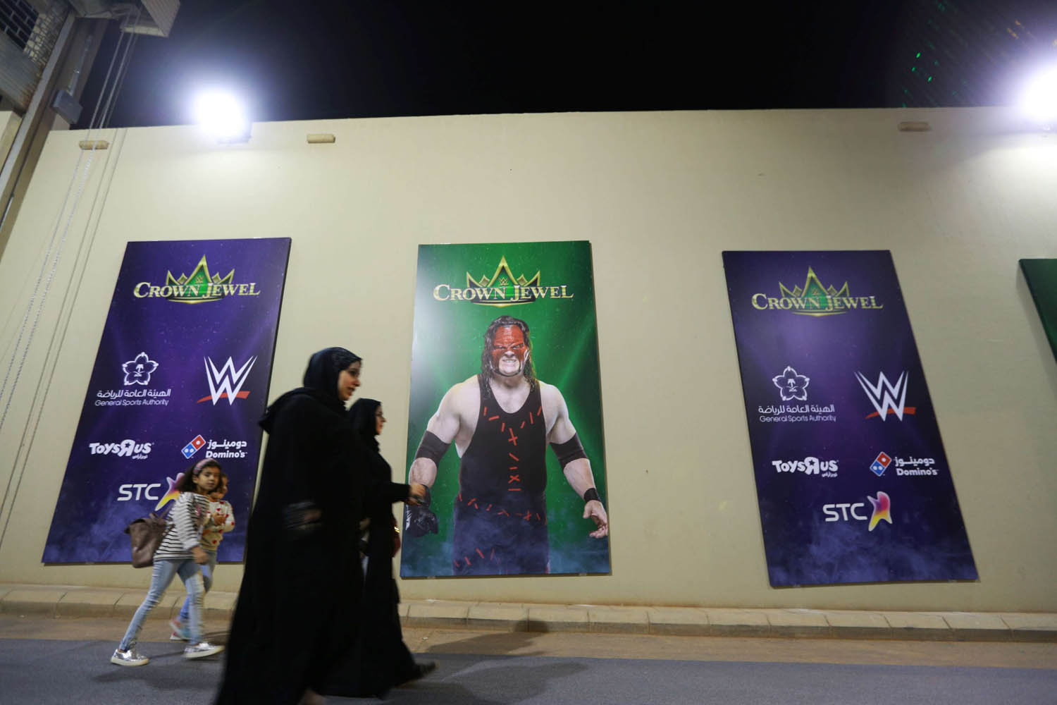 سعوديات يمررن بجانب ملصقات تعلن عن مسابقات للمصارعة الحرة