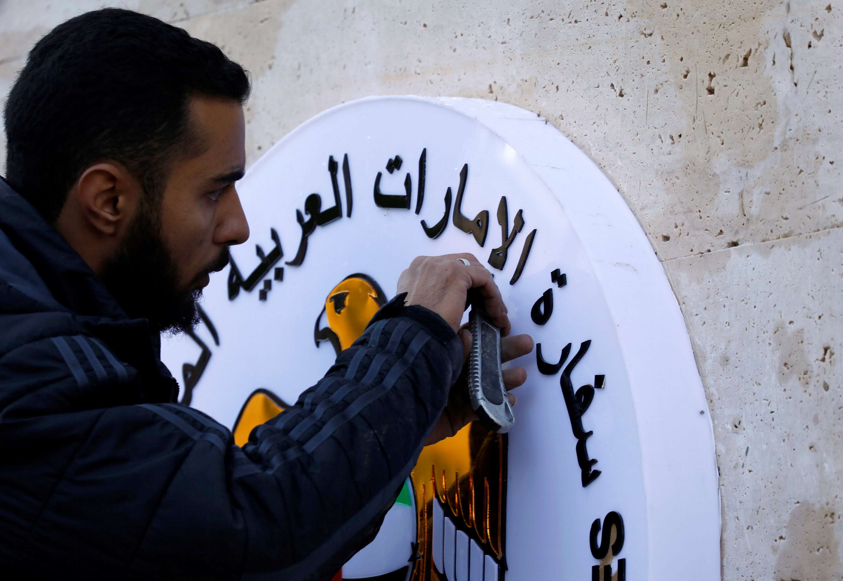 عامل يضع اللمسات الأخيرة على شعار سفارة الإمارات على الجدران الخارجية قبل الافتتاح