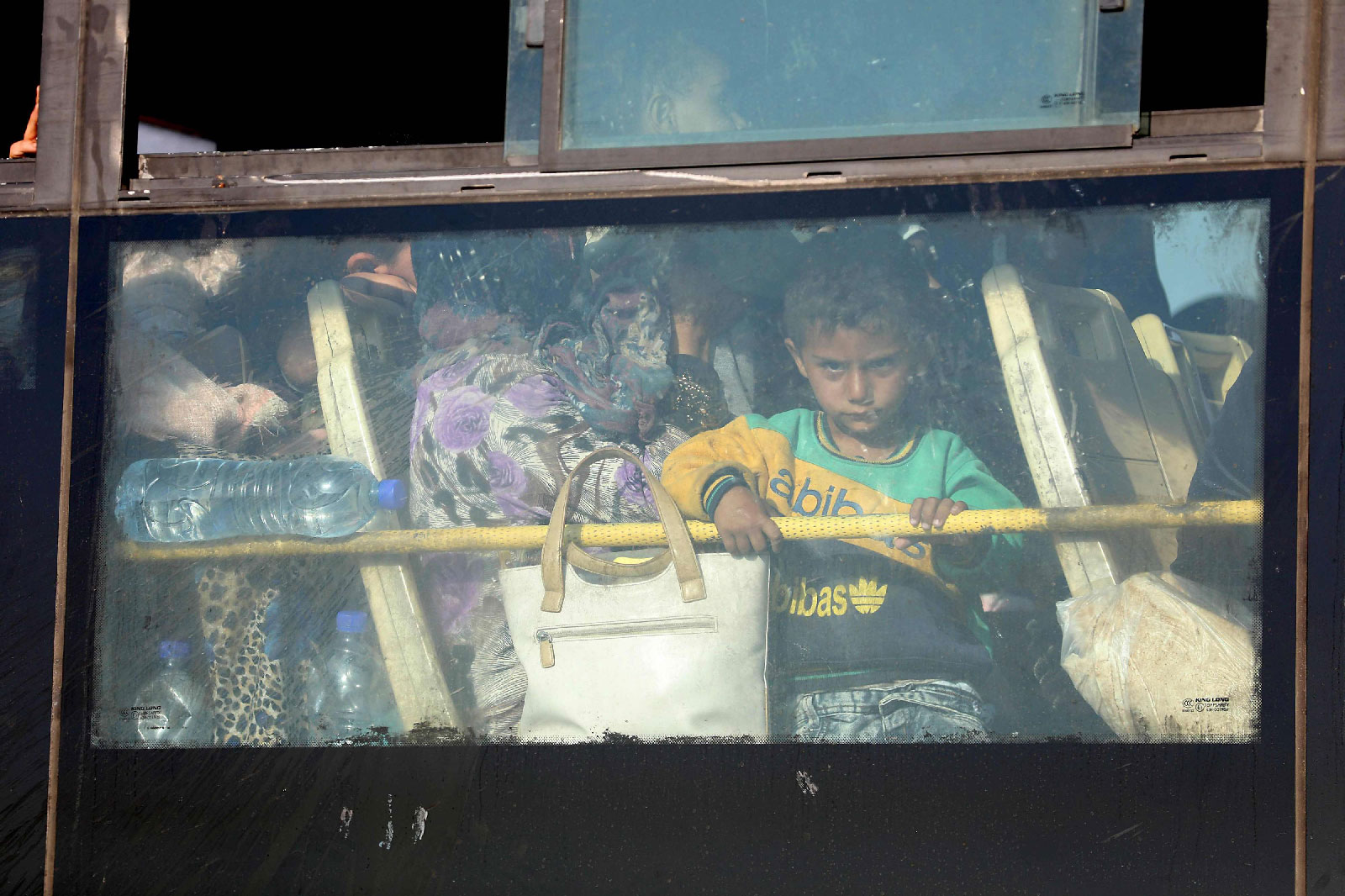 A Syrian child looks through the windows of a bus as displaced people from the Quneitra province wait at the Murak crossing point to be carried in the provinces of Idlib and Aleppo, in Murak, northwestern Syria, on July 21, 2018.