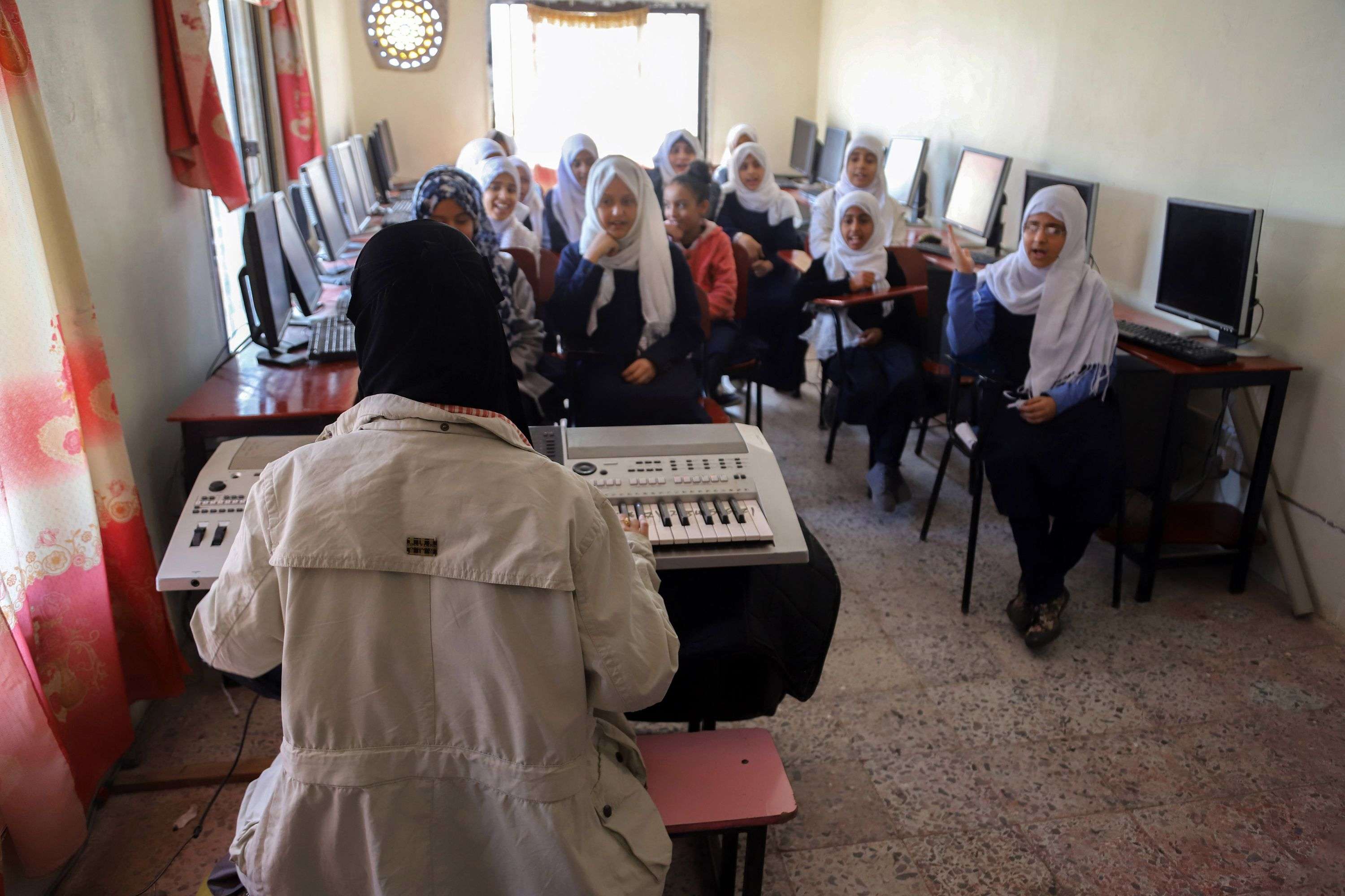 Smiling and tapping on their desks, a class of bright-eyed students sing, in English, "My face, my face, this is my nose".
