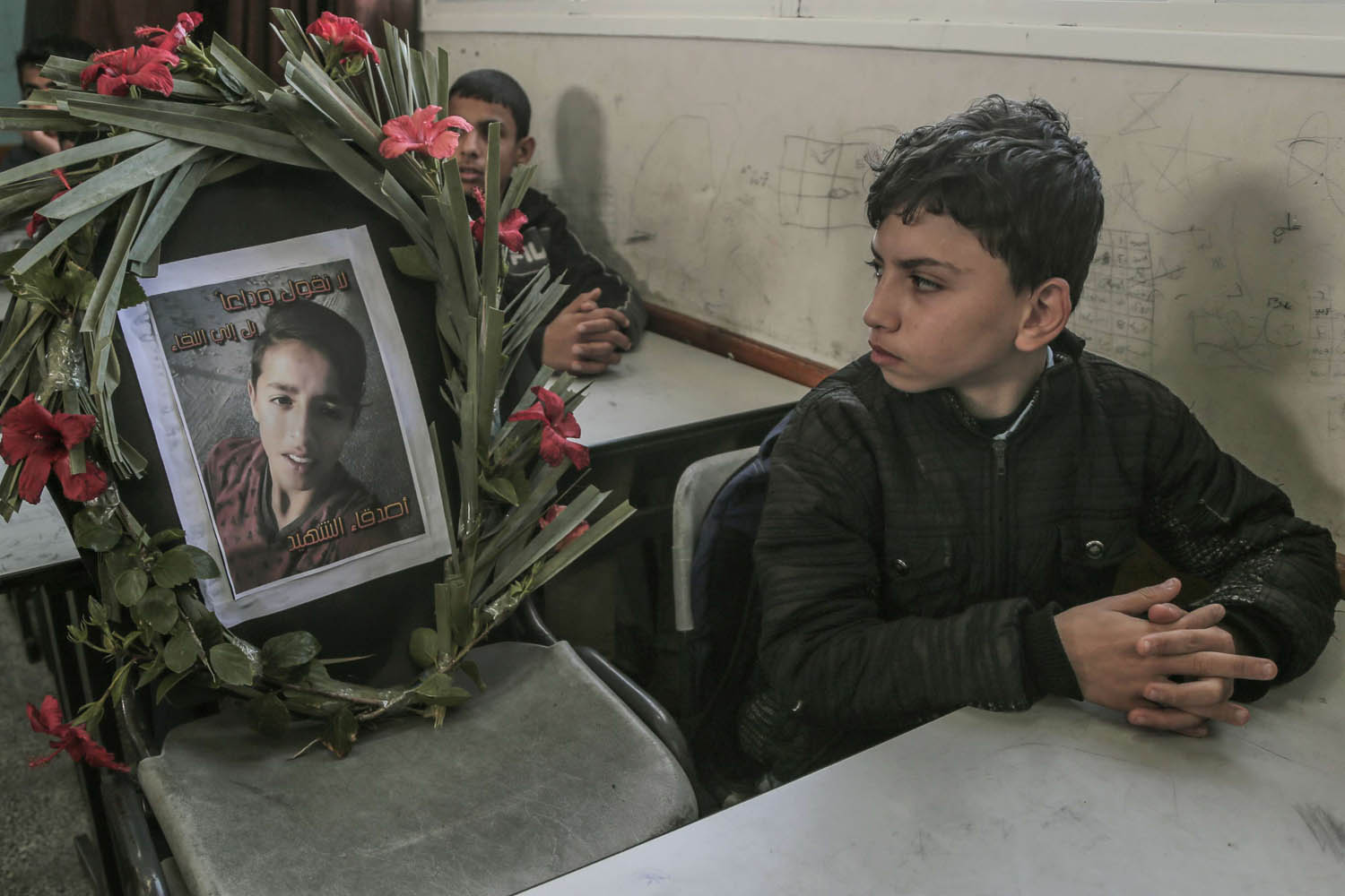طفل فلسطيني ينظر إلى صورة زميله الشهيد في مدرسة في غزة