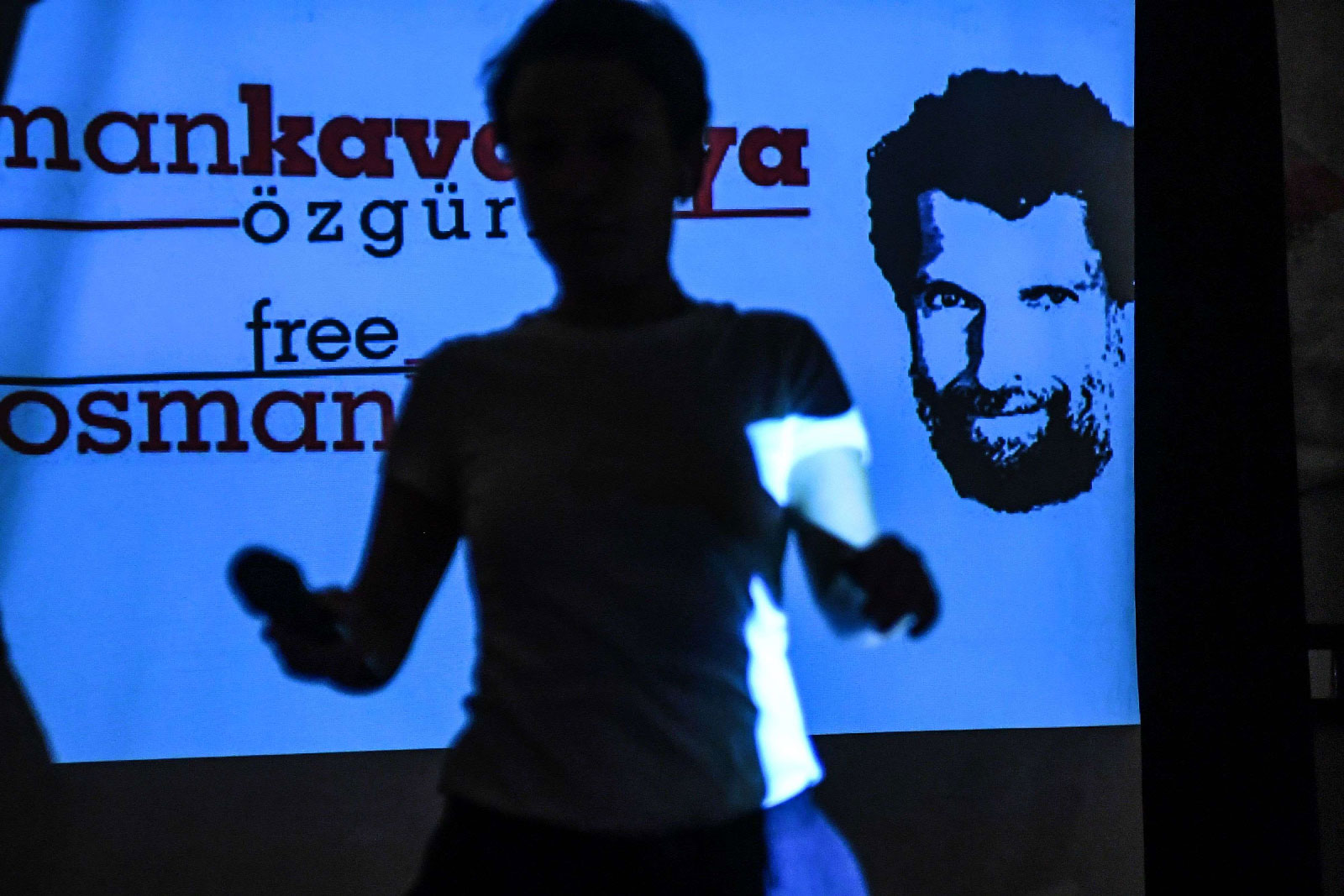 A woman passes in front of a screen featuring jailed businessman and philanthropist Osman Kavala during a press conference of his lawyers on October 31, 2018.
