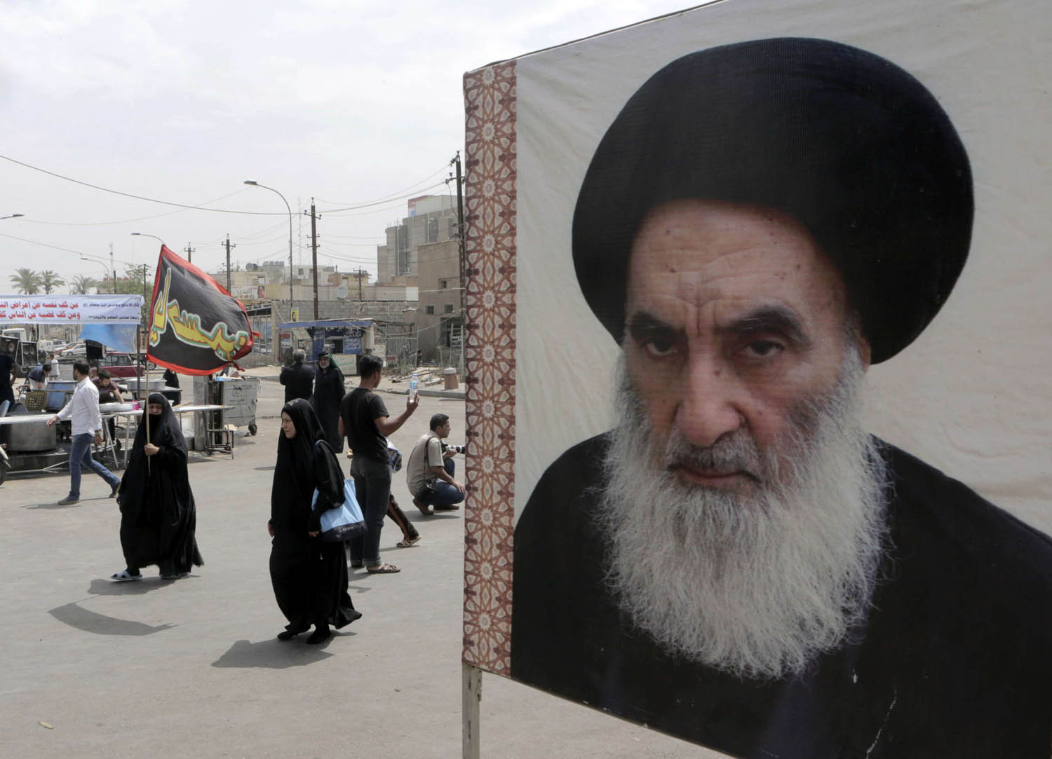 عراقيات يمررن بقرب ملصق للمرجع الشيعي علي السيستاني في بغداد