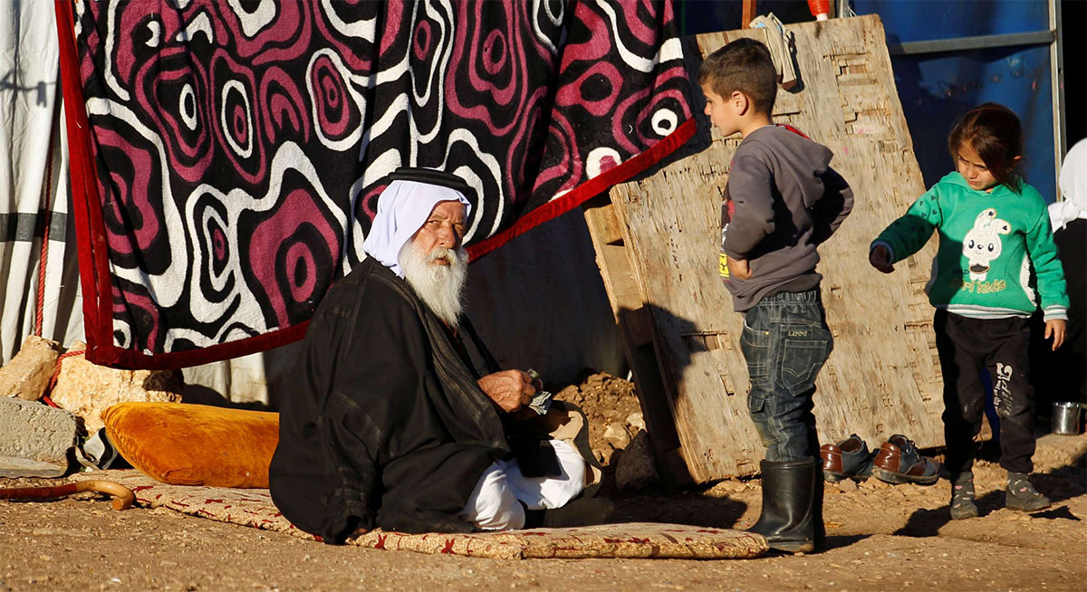 A man sits outside his tent as children look on at a refugee camp in Sinjar