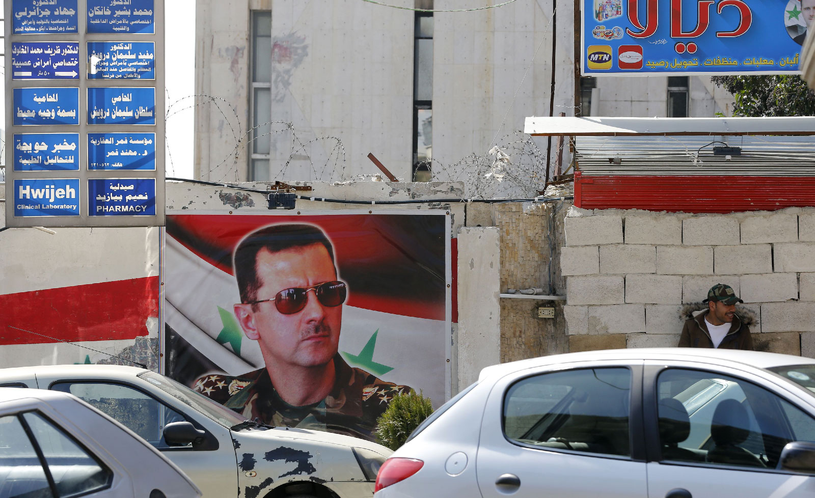 A picture taken on March 11, 2019 shows a Syrian man sitting next to a billboard bearing a portrait of President Bashar al-Assad in the capital Damascus. 