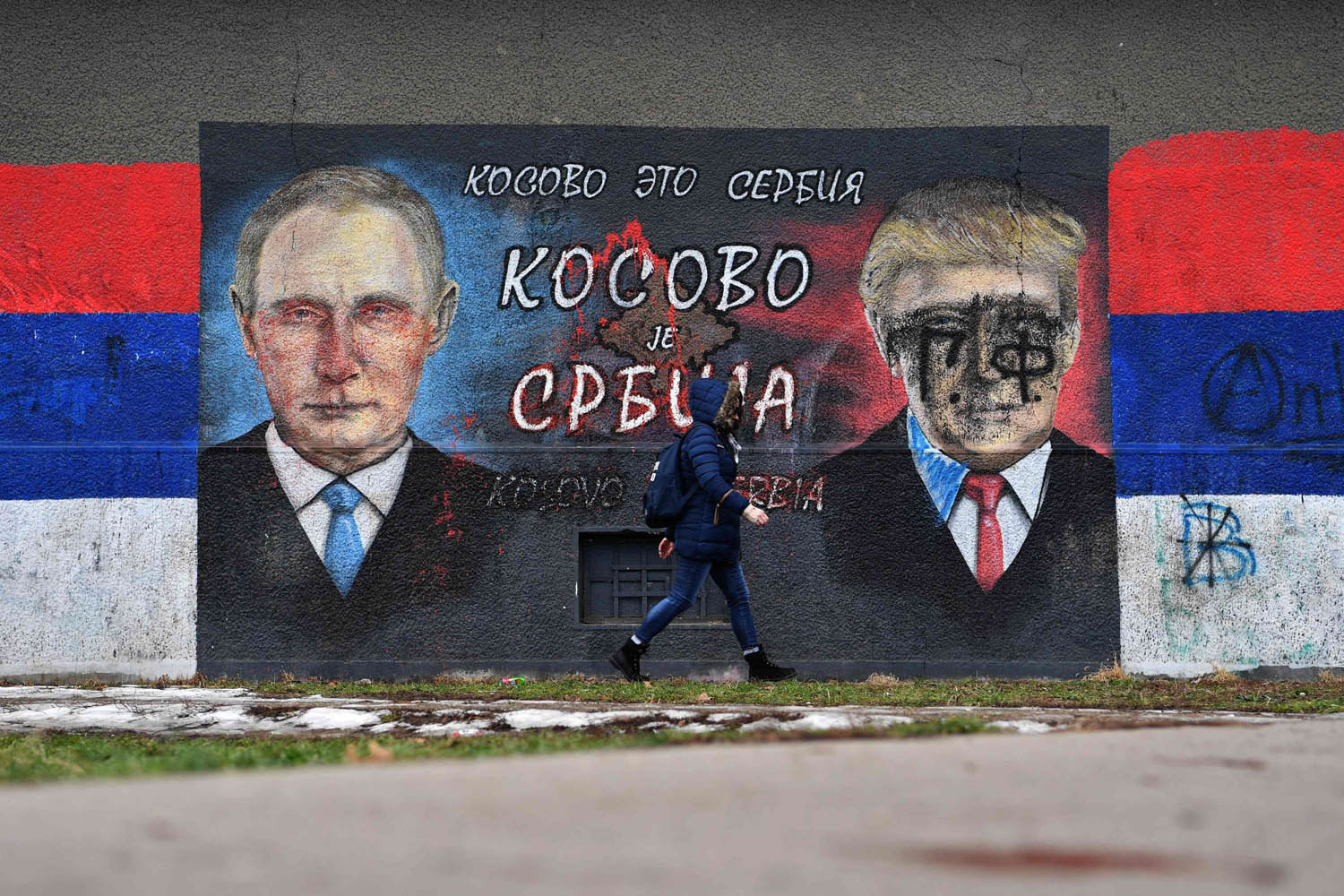 طفل صربي يمر بالقرب من جدارية تحمل صورتي الرئيس الروسي فلاديمير بوتين والأميركي دونالد ترامب