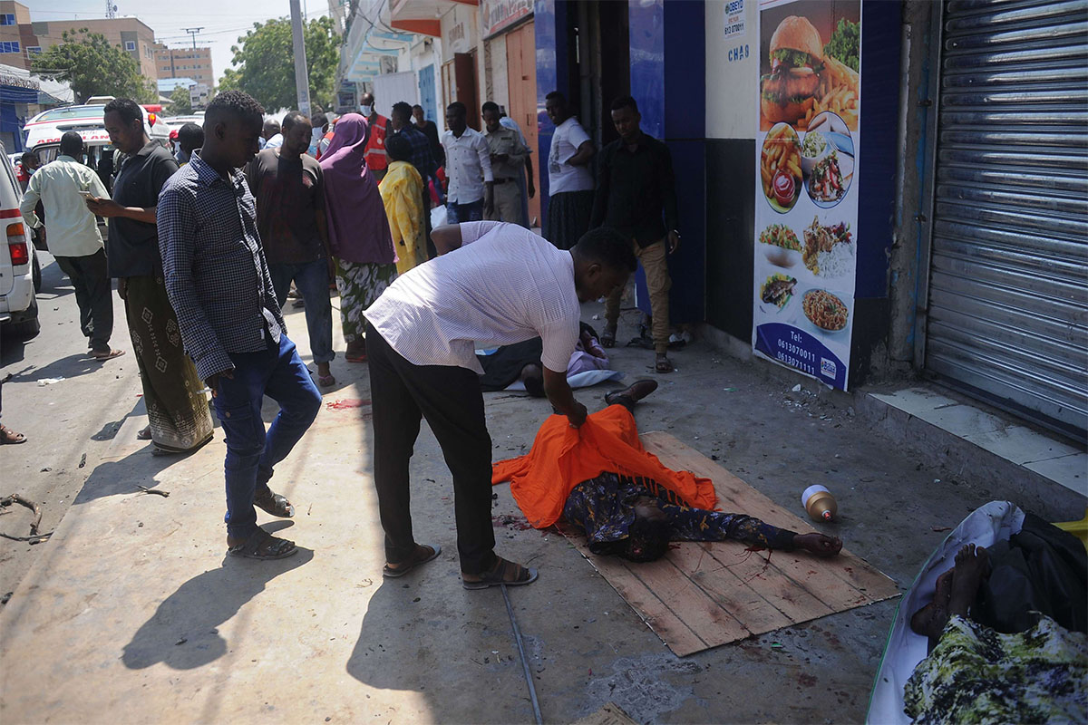 Somalis examine the dead body of a civilian killed after an explosion outside a restaurant