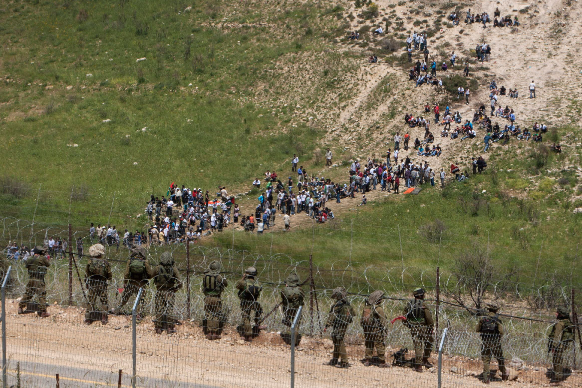 Israeli troops take positions, front, as pro-Palestinian protesters approach the border between Israel and Syria near the village of Majdal Shams in the Golan Heights.