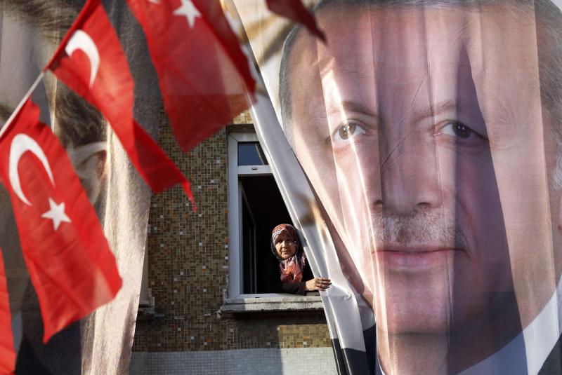 A woman peers out of her window behind a banner of Turkey’s President Recep Tayyip Erdogan in Istanbul, March 5