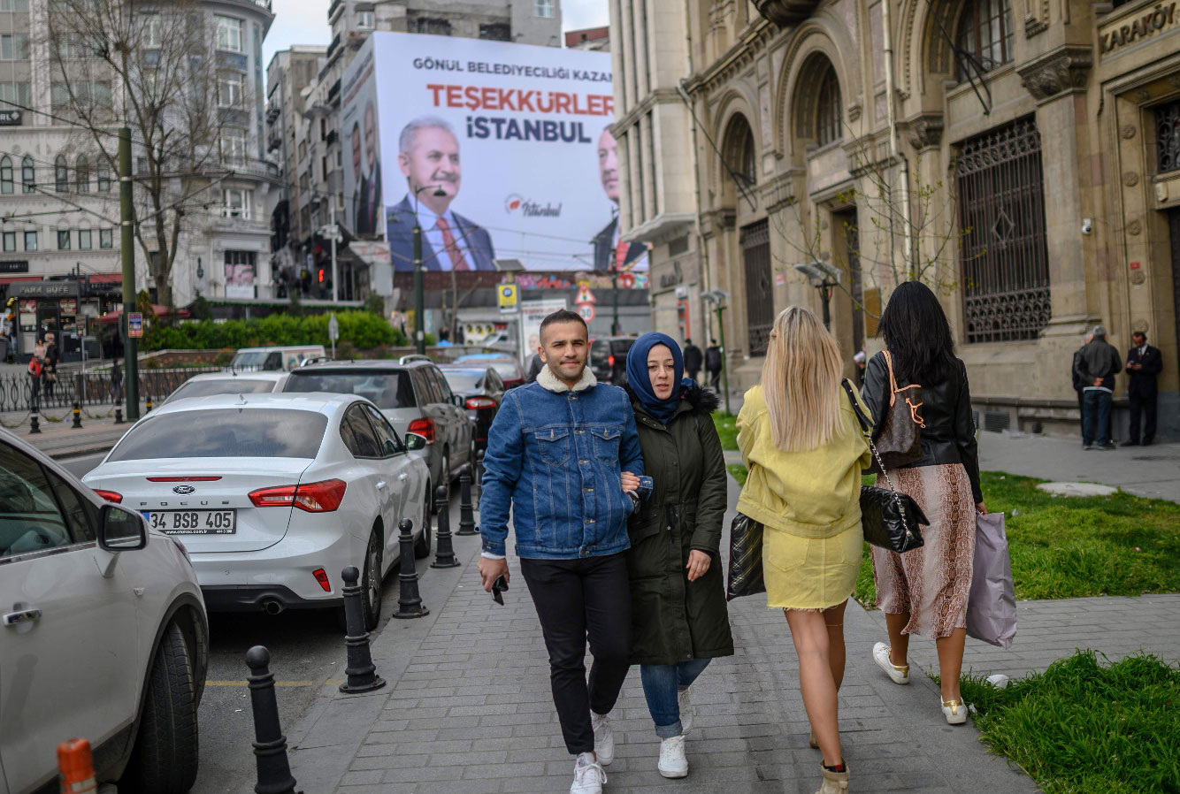 People go about their daily life next to a billboard reading "Thank You Istanbul" and portraying AKP ruling party mayor candidate Binali Yildirim and President Recep Tayyip Erdogan, in Istanbul, on April 2, 2019.