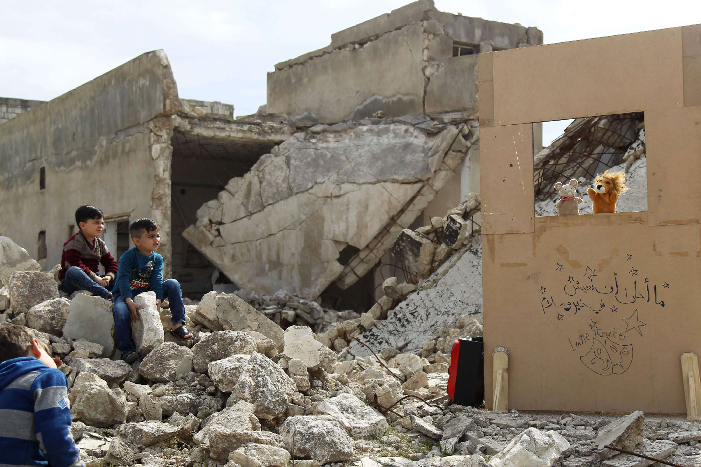 Children watch a puppet show performed by a Syrian actor, through a makeshift puppet theatre set up among the rubble of collapsed buildings in the town of Saraqib.