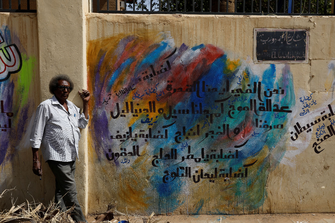 Rashid Drar, a 44-year old artist, poses next to graffiti in Khartoum