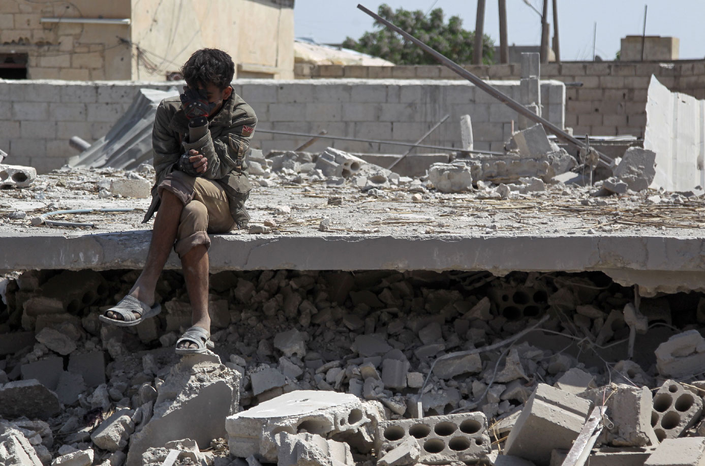 A man sits amidst the rubble of a building in Idlib, destroyed during airstrikes by the Syrian regime