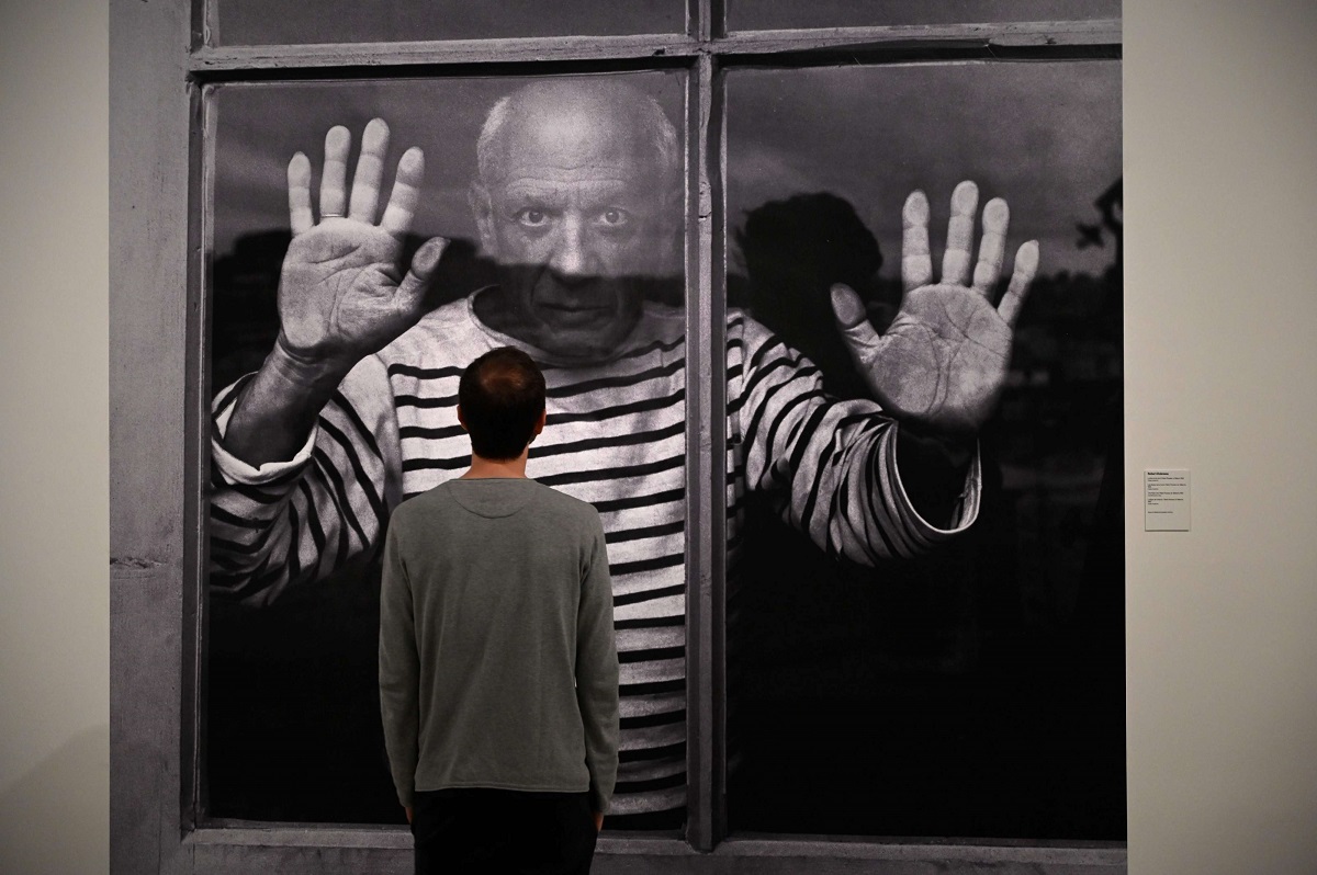 رجل ينظر إلى صورة للمصور الفرنسي روبرت دويسنو  يظهر فيها بيكاسو واقفا وراء نافذة
