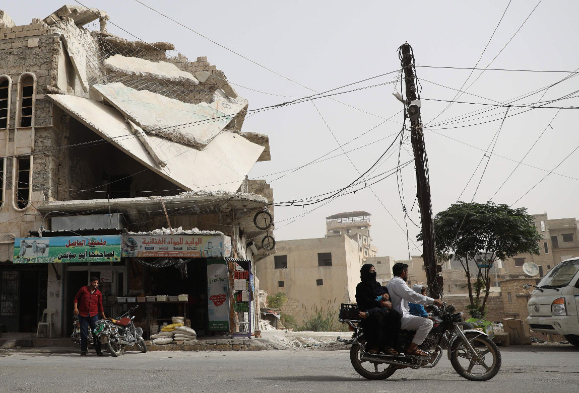 A man drives his motorcycle past a damaged building in the town of Binnish