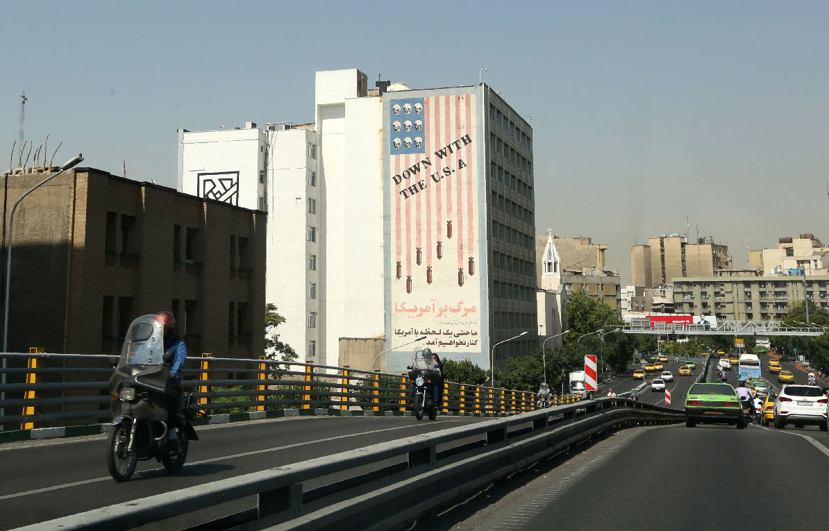 Cars drive past mural painting along the wall of a building in the Iranian capital Tehran
