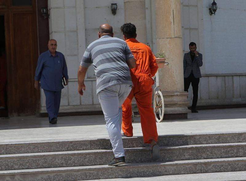 An Islamic State suspect wearing a red prison suit is led to the Iraqi Criminal Court in Baghdad