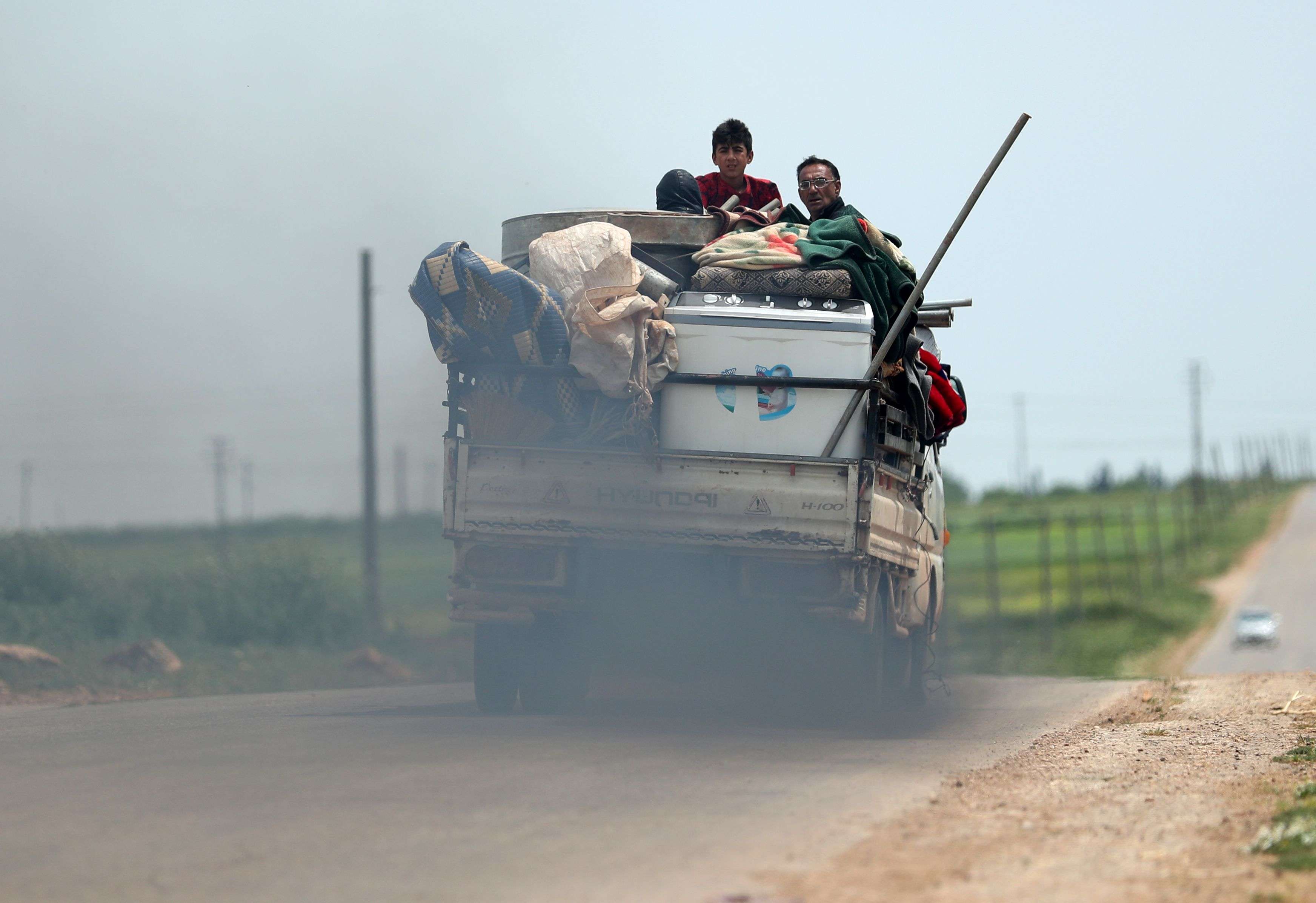 A displaced Syrian family rides in the back of a truck loaded with furniture and clothes