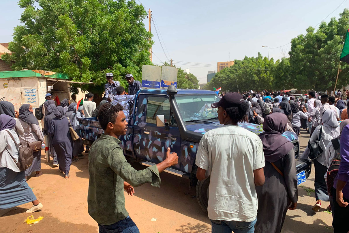 Sudanese protesters march past security forces' vehicle during a demonstration commemorating protesters killed