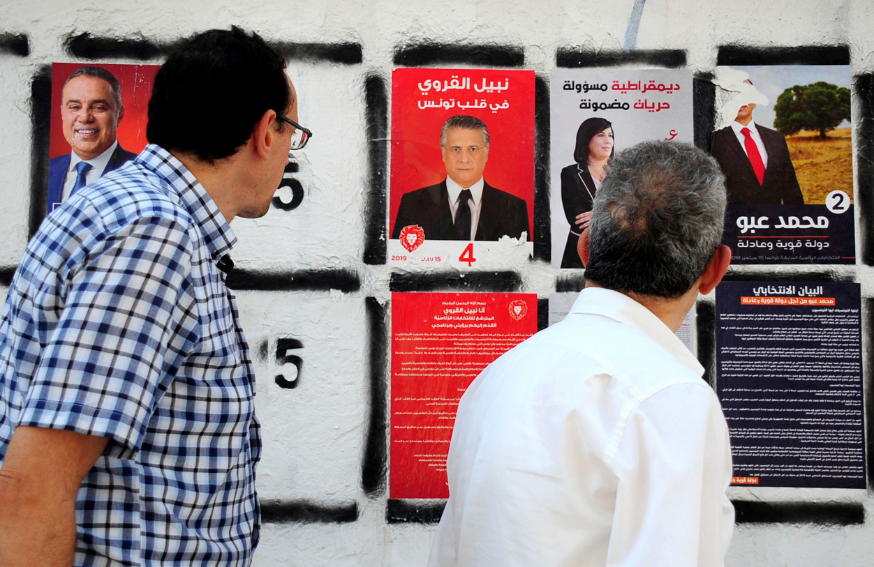 Men watch a campaign poster of the owner of the Tunisian private channel Nessma TV, Nabil Karoui (C)