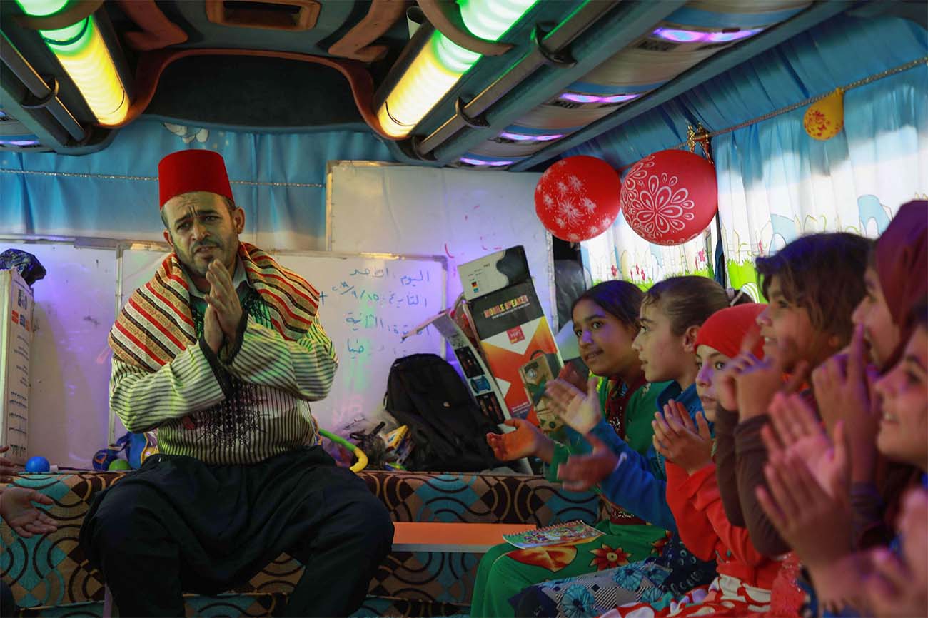 Displaced Syrian children sing on a bus converted into a classroom near the village of Hazano in northwestern Syria