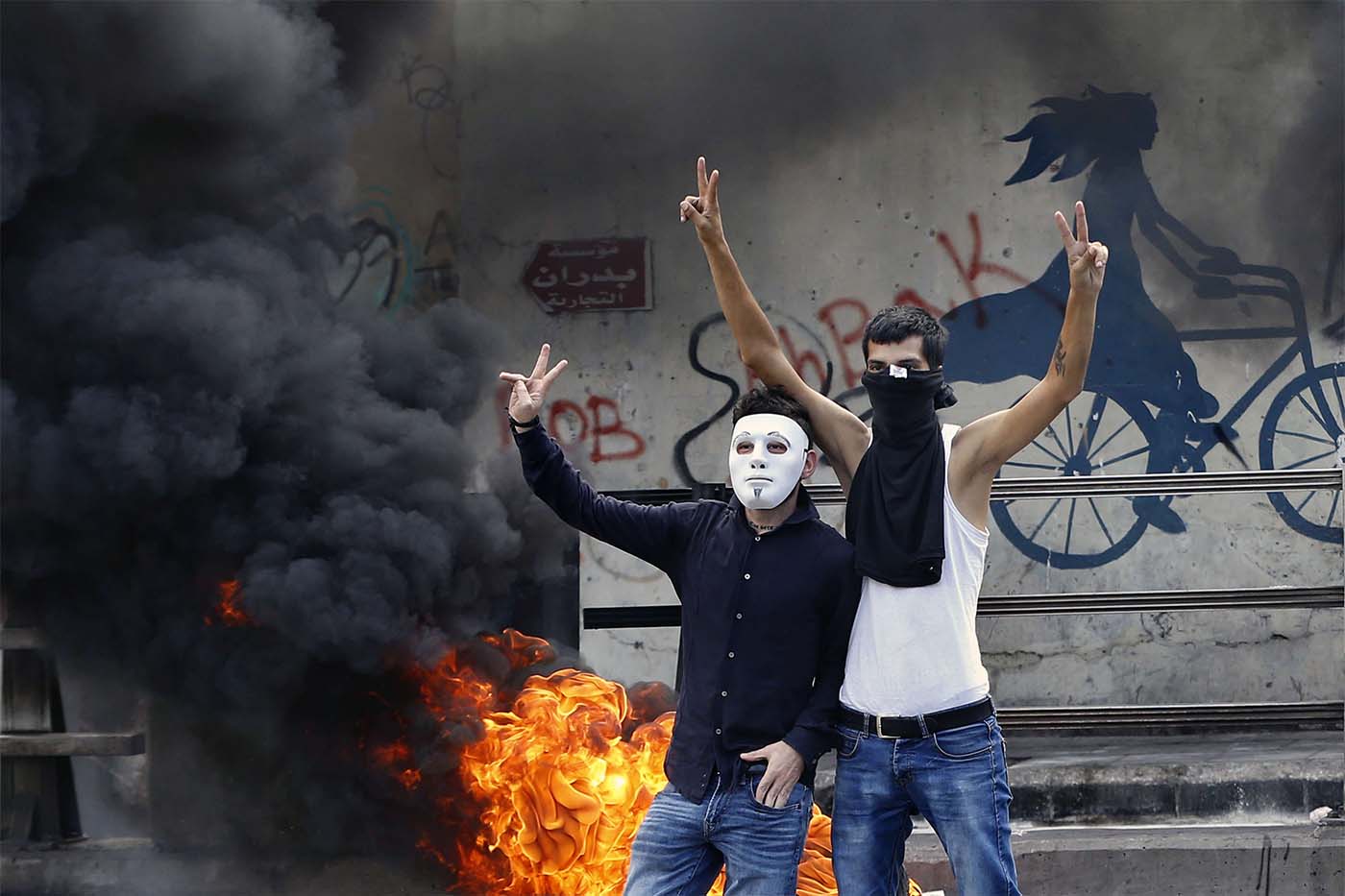 Anti-government protesters make victory signs next to tires that were set on fire to block a road during a demonstration, in Beirut
