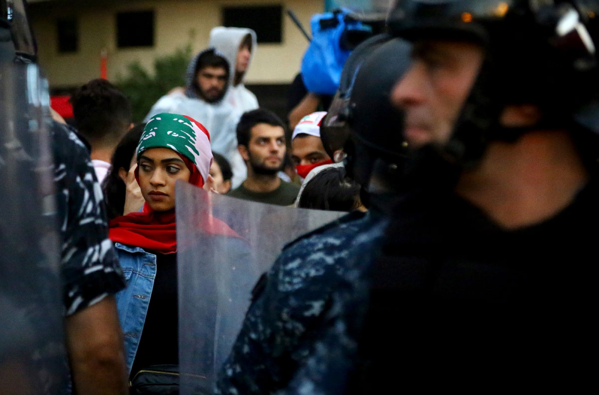 A demonstrator stands behind riot police during a protest at Riad al-Solh square in Beirut