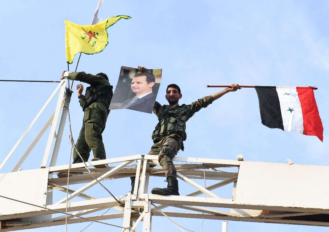 A Syrian government soldier holds up a portrait of President Bashar al-Assad and a Syrian national flag while another stands by a Kurdish YPG flag