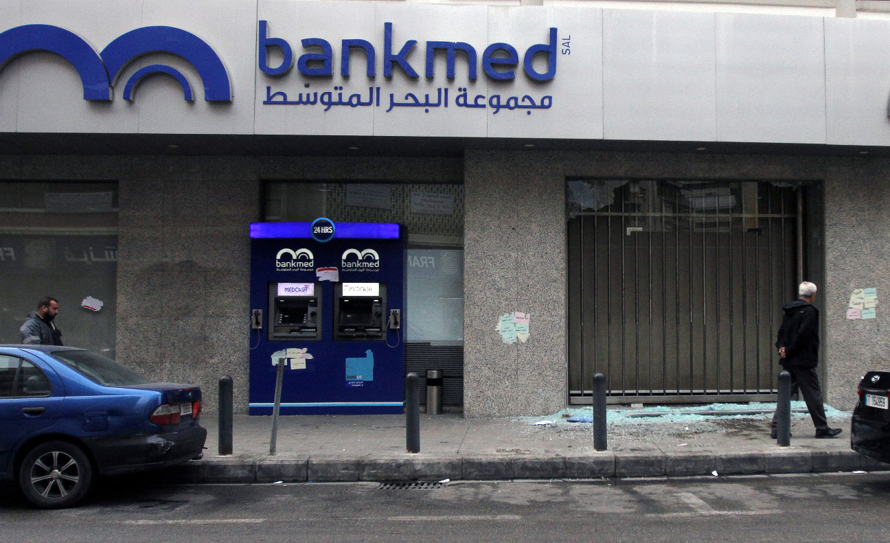Men walk near broken glass from a damaged Bankmed branch in Tripoli, Lebanon