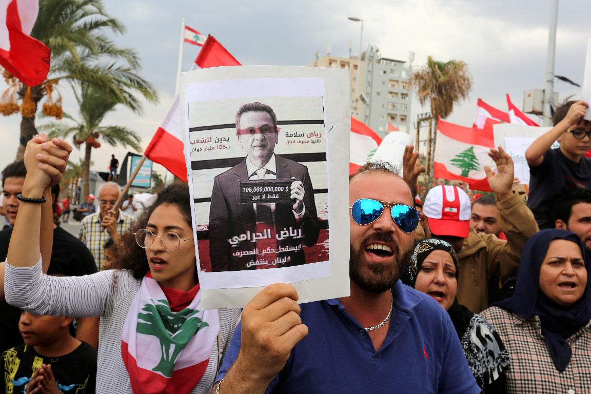 Demonstrators carry Lebanese flags and a banner depicting Lebanon's Central Bank Governor Riad Salameh