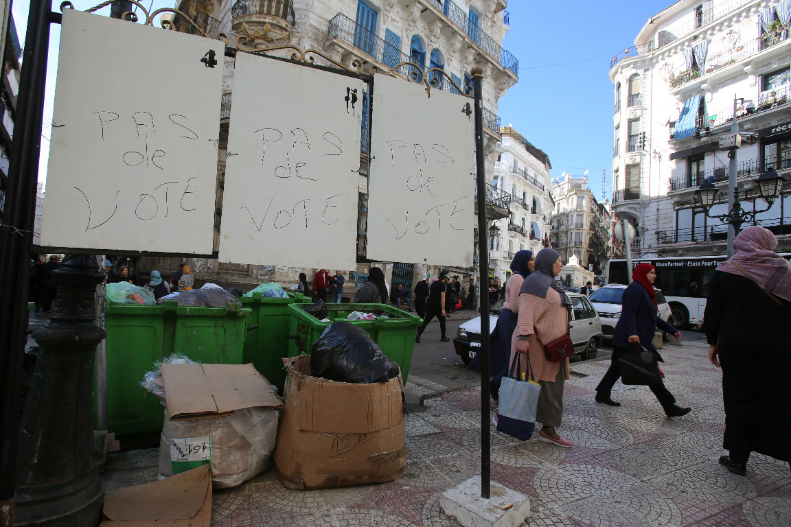 "No vote" reads on electoral panels as women walk past in Algiers