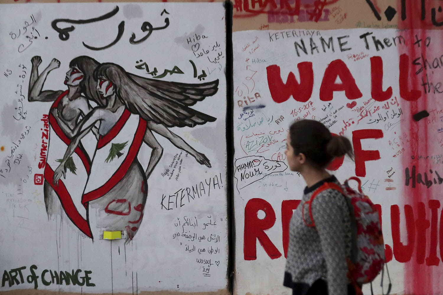 لبنانية تمر بجانب غرافيتي عن الثورة في لبنان