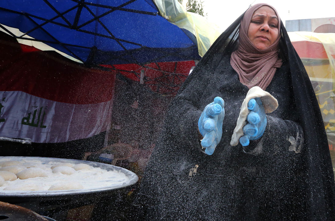 An Iraqi woman prepares traditional bread on the sidelines of ongoing anti-government protests at Tahrir square