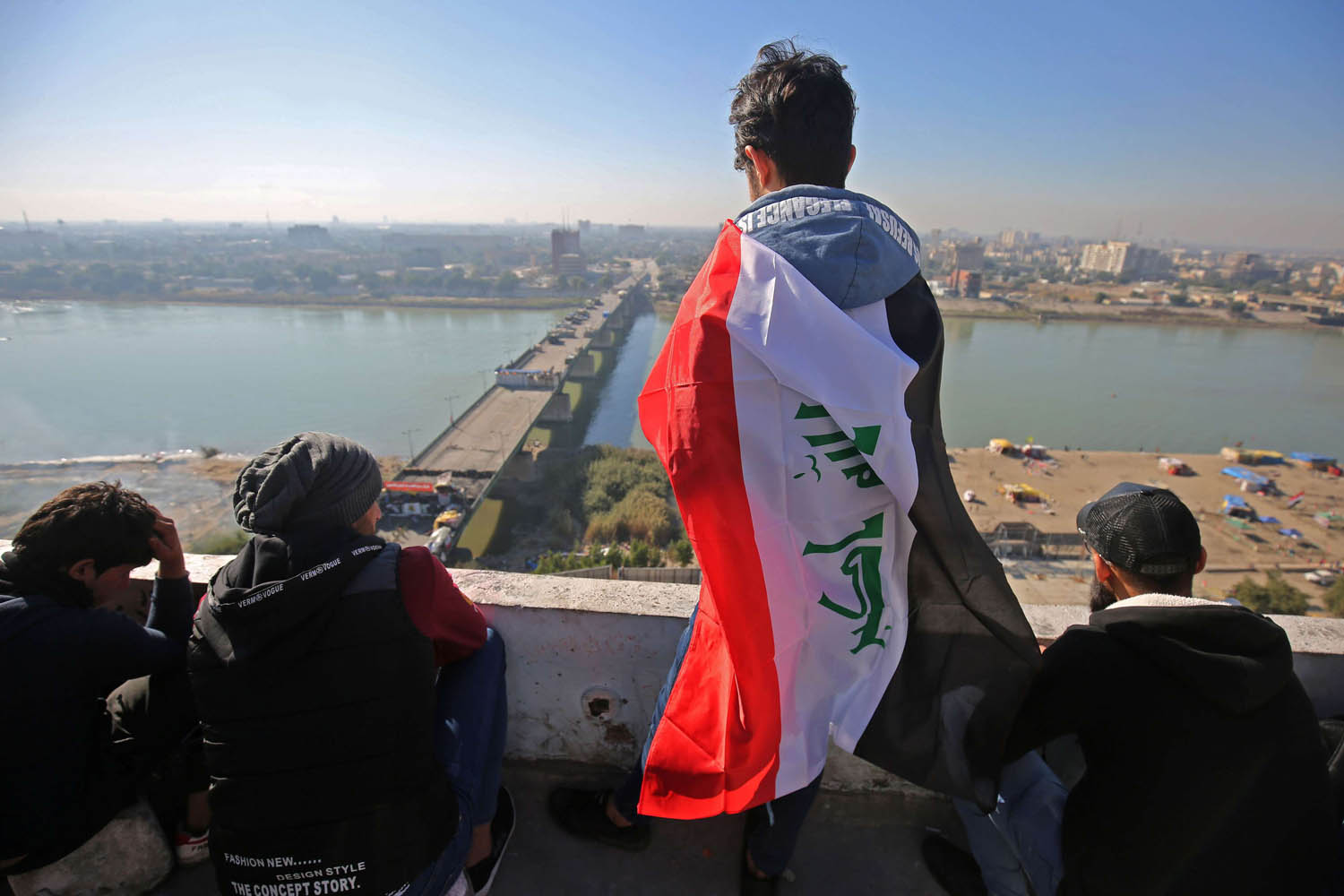 عراقي يتلفح بعلم فوق مبنى يطل على جسر الجمهورية وسط بغداد