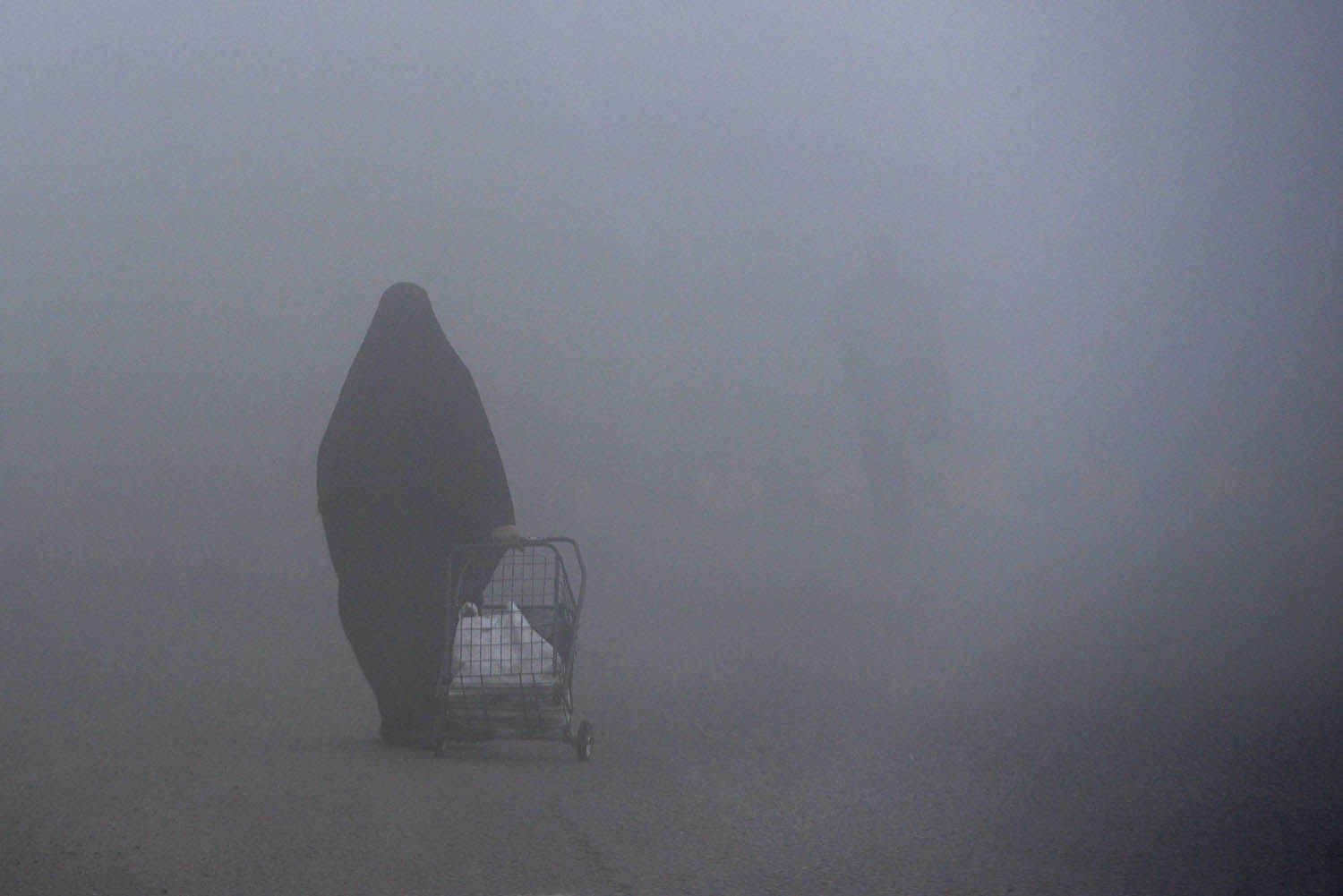 عراقية تمشي وسط الضباب في بغداد
