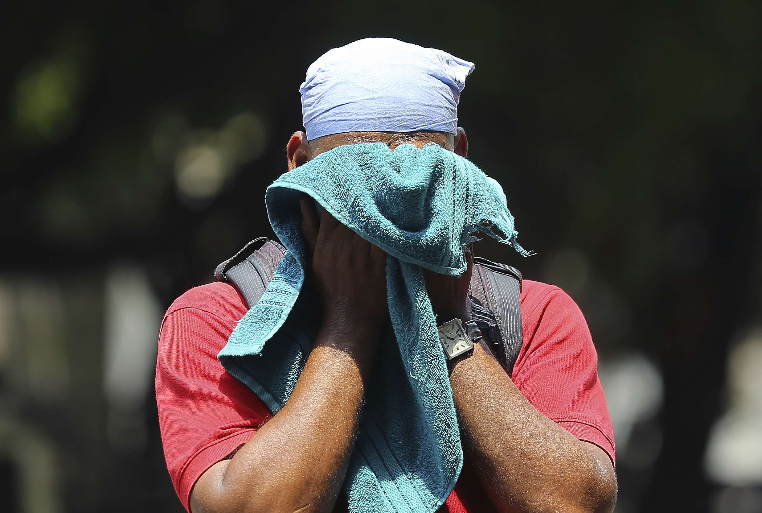 رجل هندي يستخدم منشفة لمسح العرق على وجهه في يوم صيفي حار ورطب في حيدر أباد بالهند