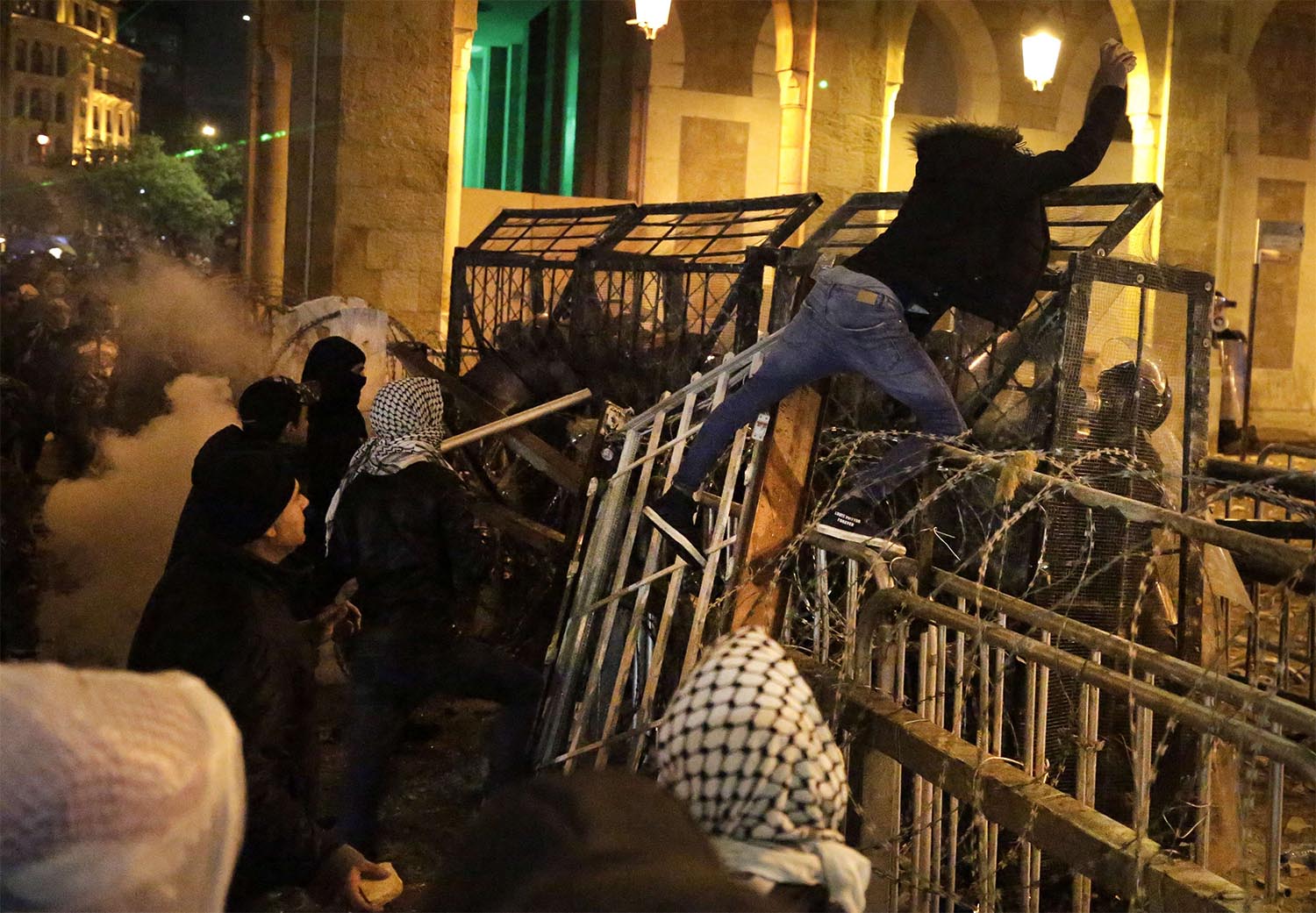 An anti-government protester stands on barriers defense as he throws stones against the riot police in Beirut