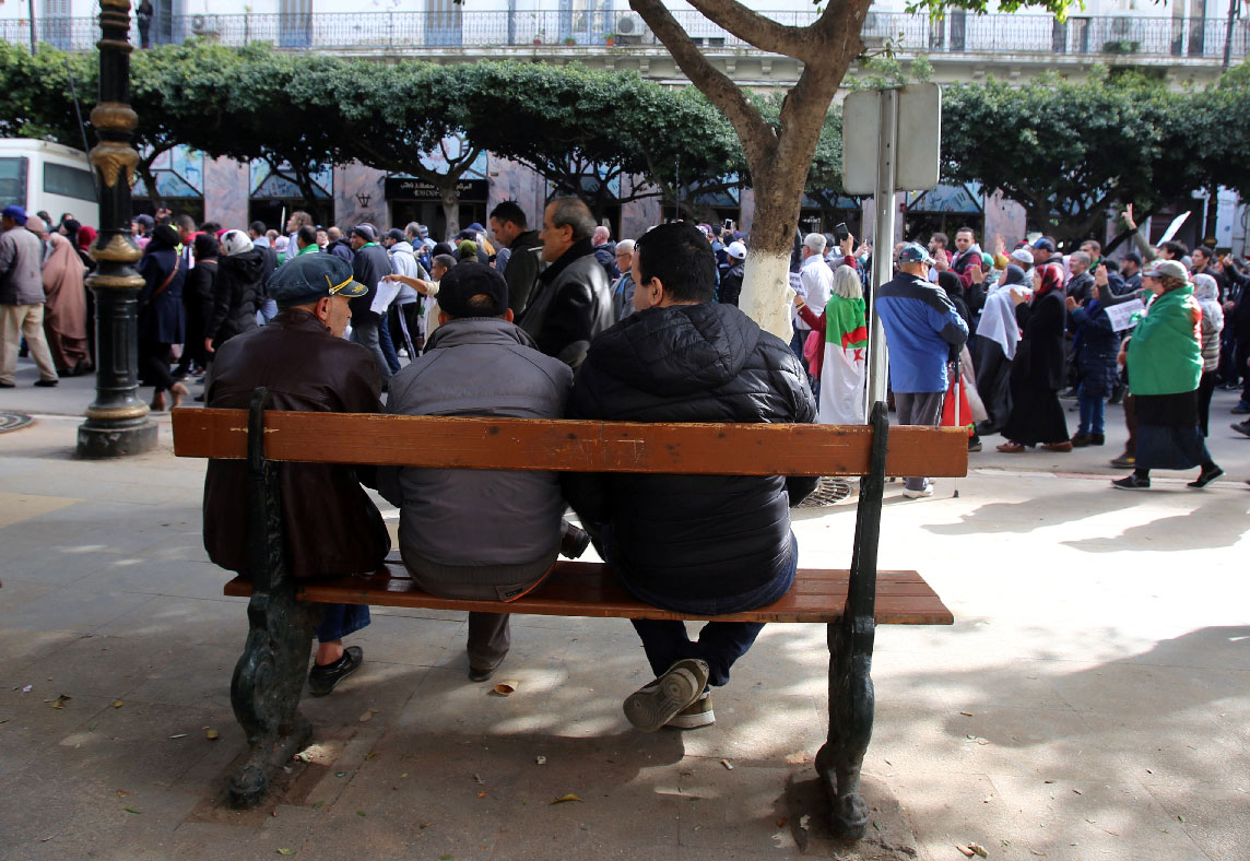 People sit on a bench as protesters demanding a change of the power structure march in Algiers