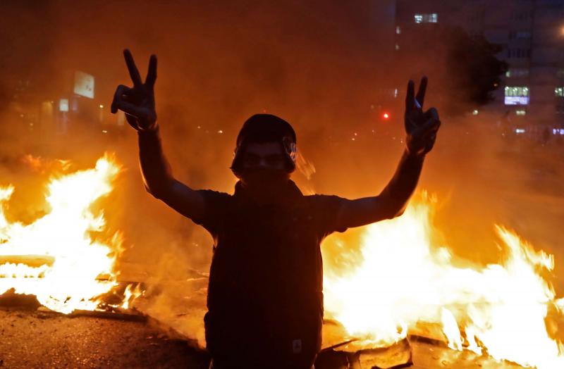 A Lebanese anti-government protester flashes the victory sign in front of a burning barricade in Beirut